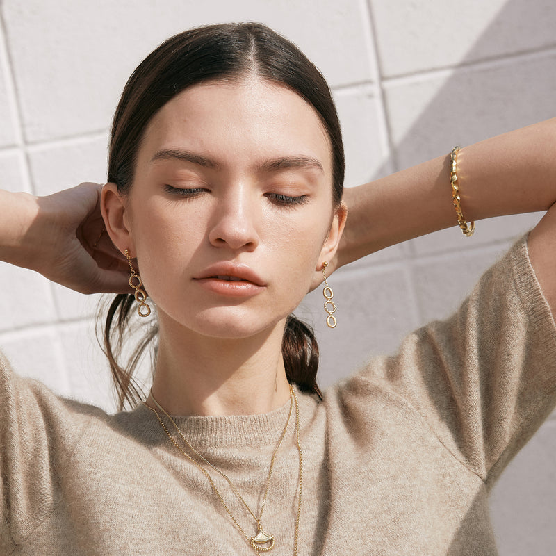 Model wearing Moyoura Connected Ovals Drop Gold Earrings with layered gold necklace and gold bangle bracelet